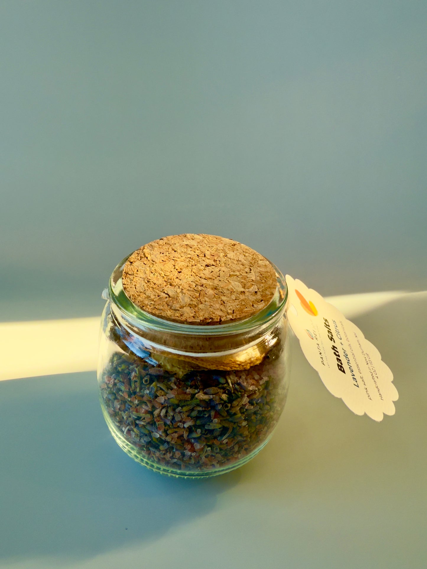 Side view of Lavender + Citrus bath salts jar showing botanicals and cork top.