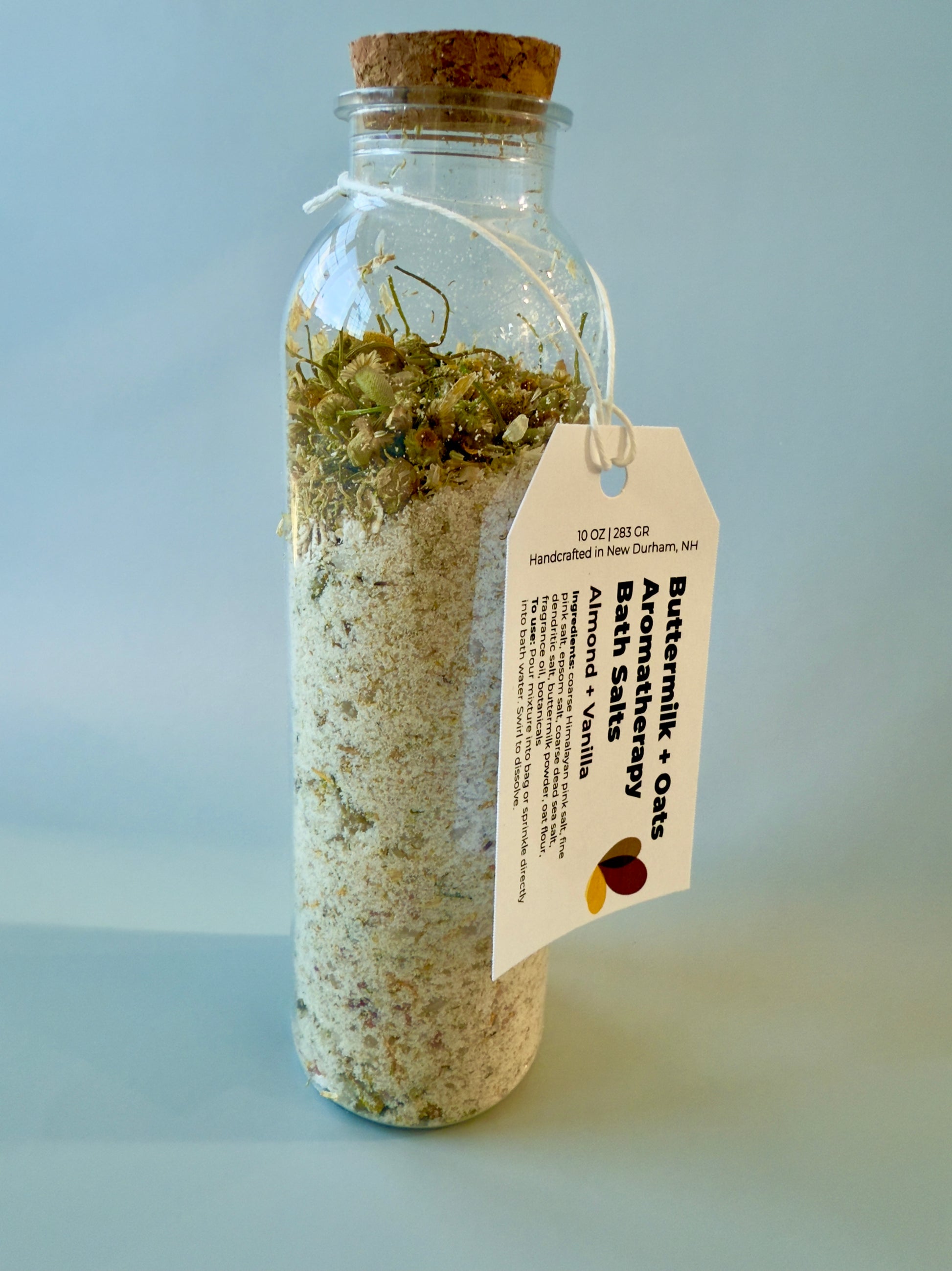 Close-up of Almond + Vanilla bath salts bottle with botanical layer and product tag.