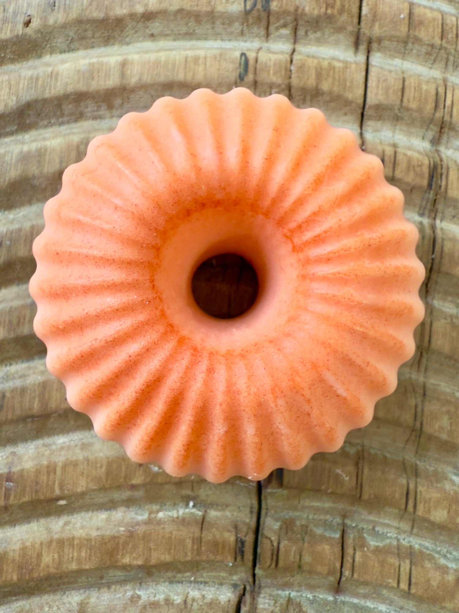 Bright orange ridged donut-shaped shampoo bar on wood background.