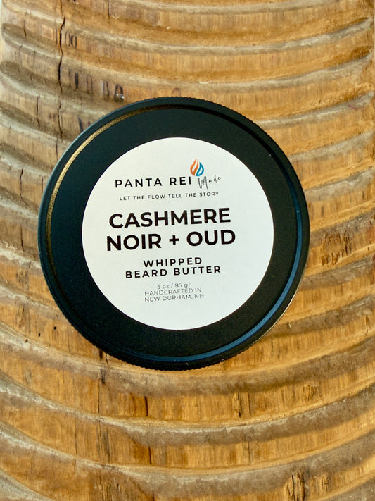 Cashmere Noir + Oud whipped beard butter jar with black lid on carved wood background.
