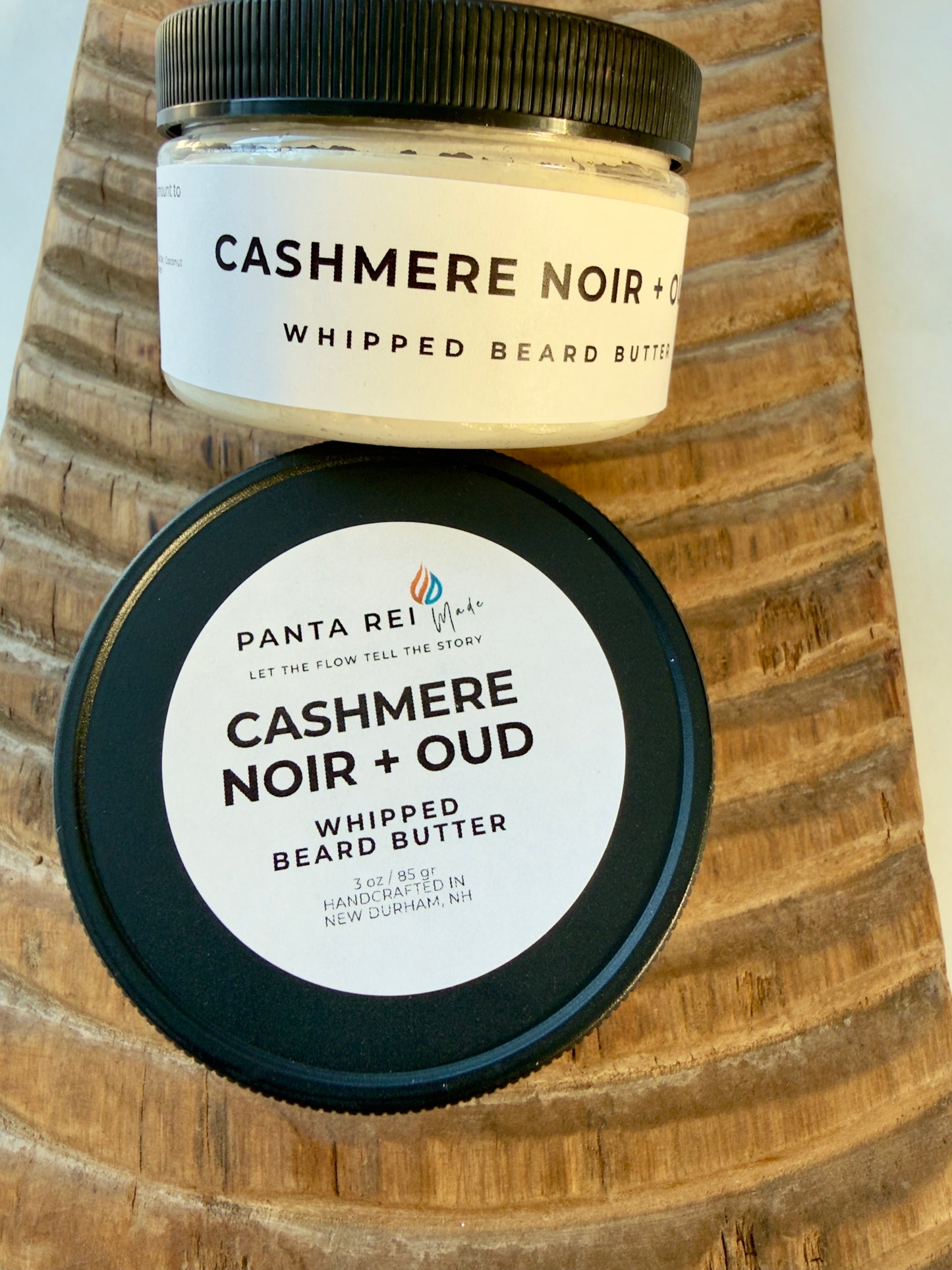 Cashmere Noir + Oud whipped beard butter jar with black lid on carved wood background.