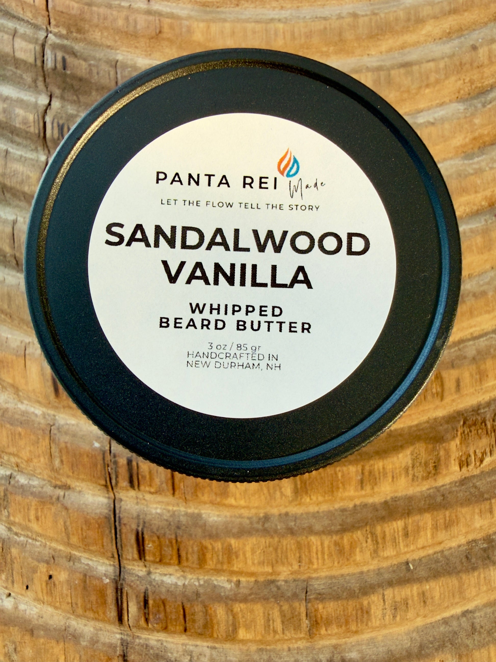Sandalwood Vanilla whipped beard butter in matte black-lidded jar on carved wood background.