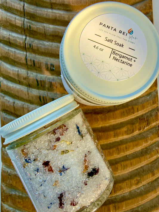 Glass jar of Bergamot + Nectarine Salt Soak with botanicals on carved wood background and white lid.