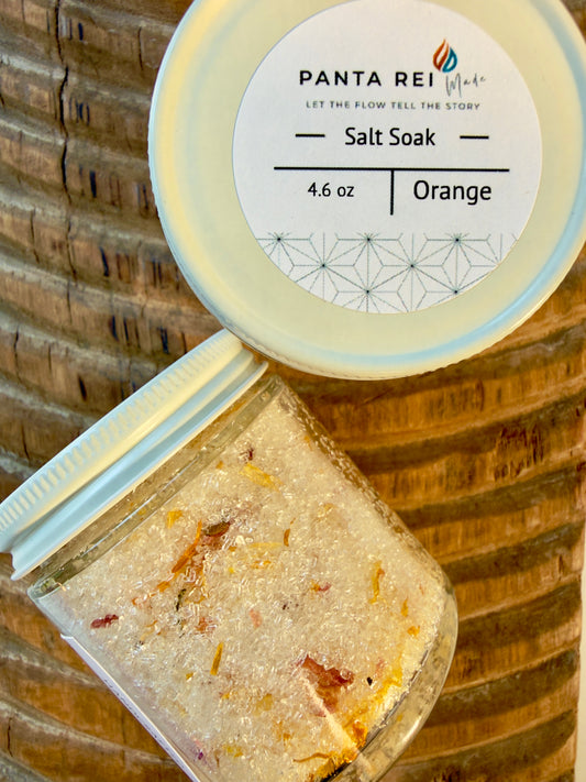 Glass jar of Orange Salt Soak with botanicals, displayed on carved wood background with matching white lid.