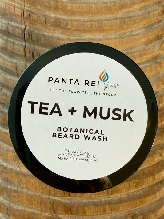 Tea + Musk Botanical Beard Wash jar with black lid on carved wood background.