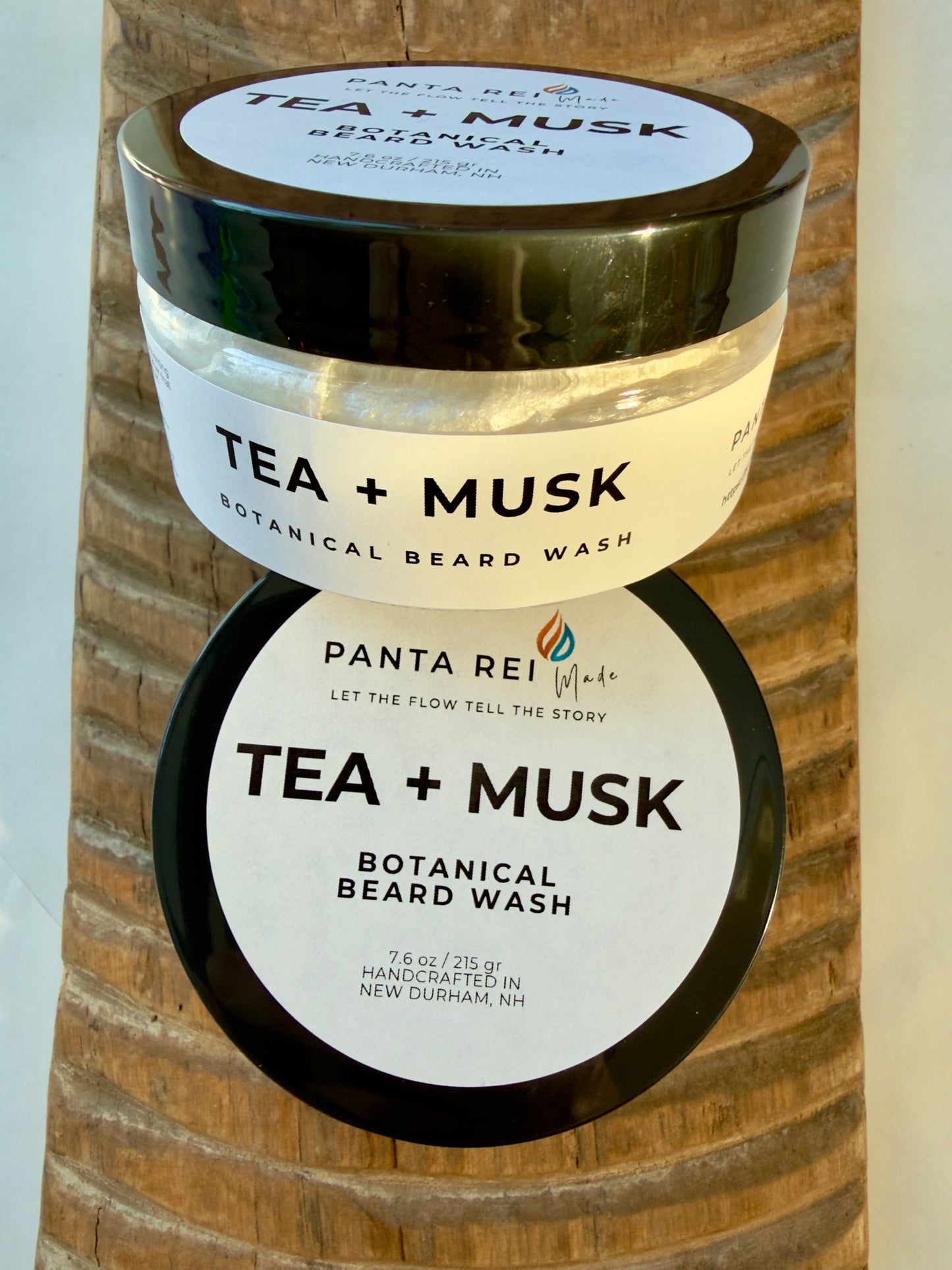 Tea + Musk Botanical Beard Wash jar with black lid on carved wood background.
