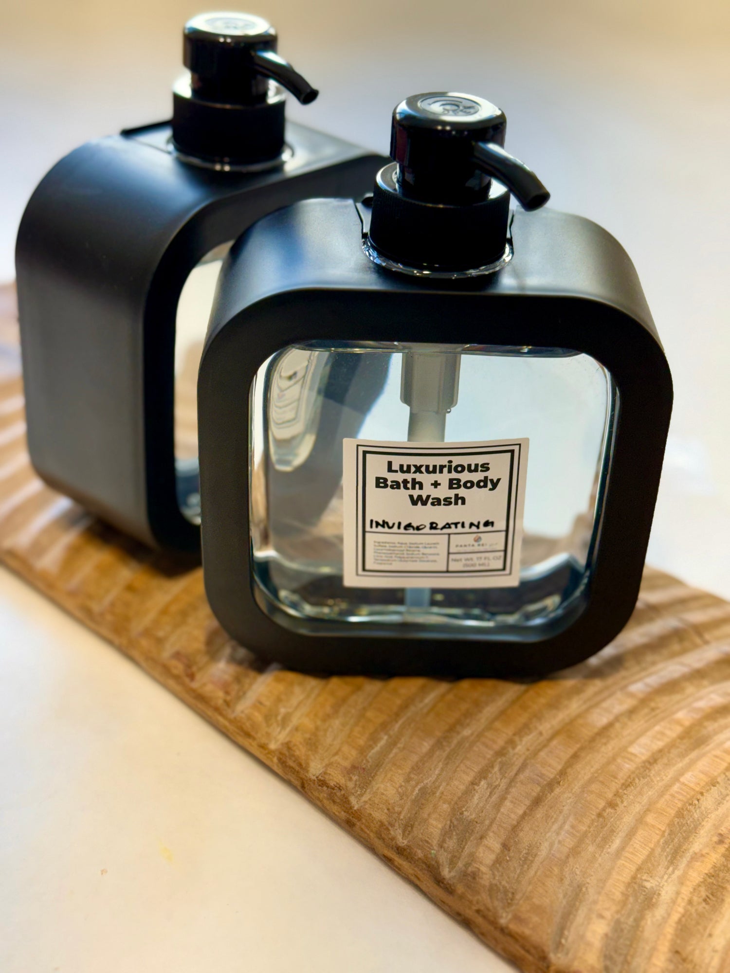 Two Invigorating Bath + Body Wash bottles displayed on a wooden board