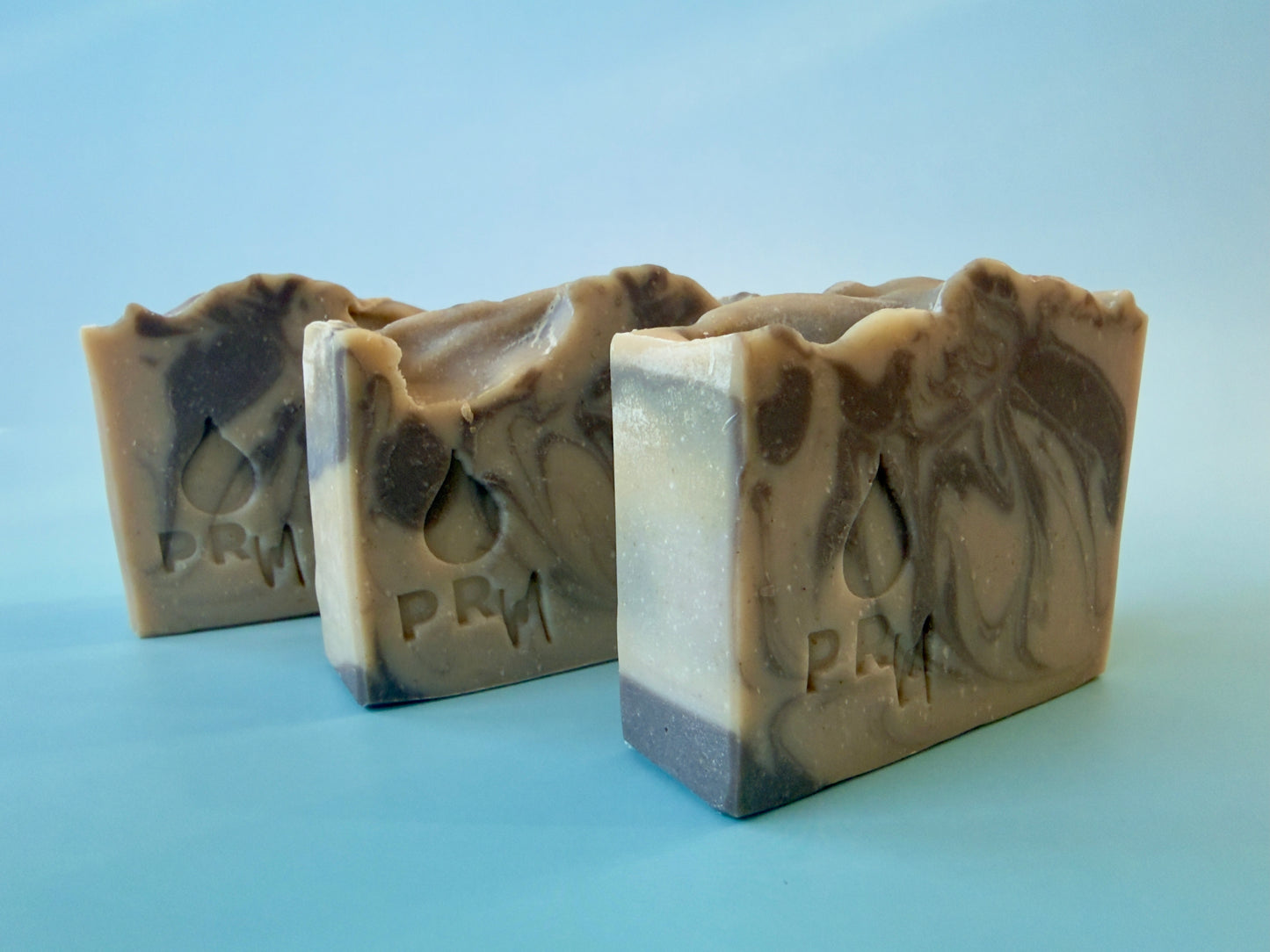 3 soap bars with warm brown and cream marbling and PRM logo on blue background