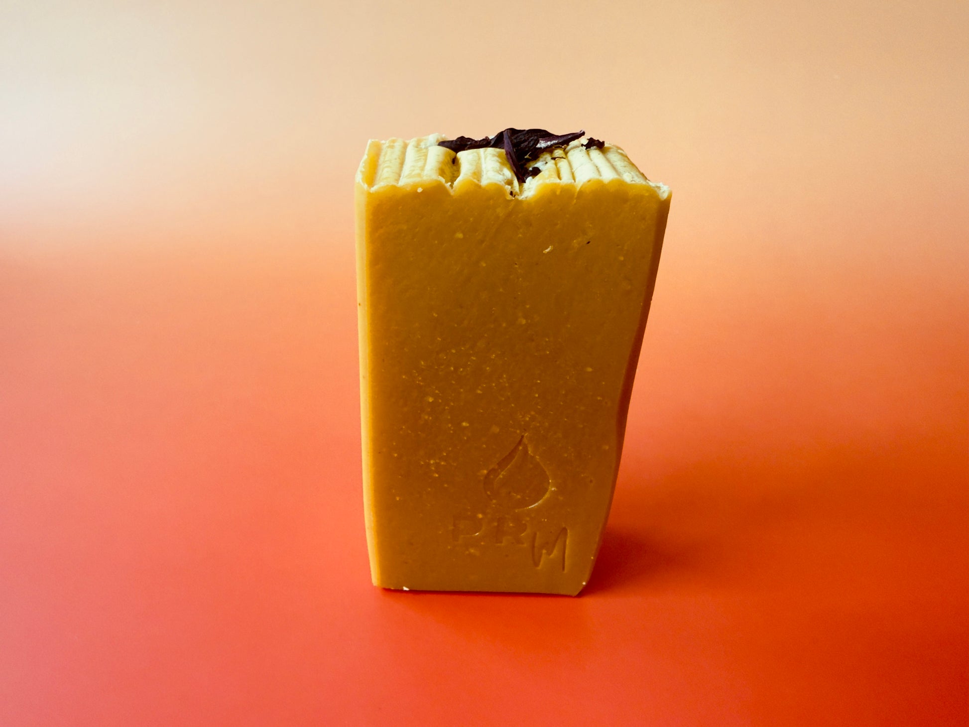 Apple Wisteria soap bar standing upright on a peach-to-pink gradient background, warm golden tone with PRM stamp