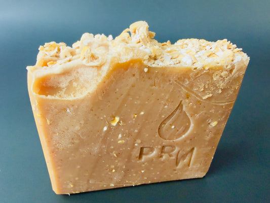 Honey Almond soap bar with oat-topped surface on dark teal background
