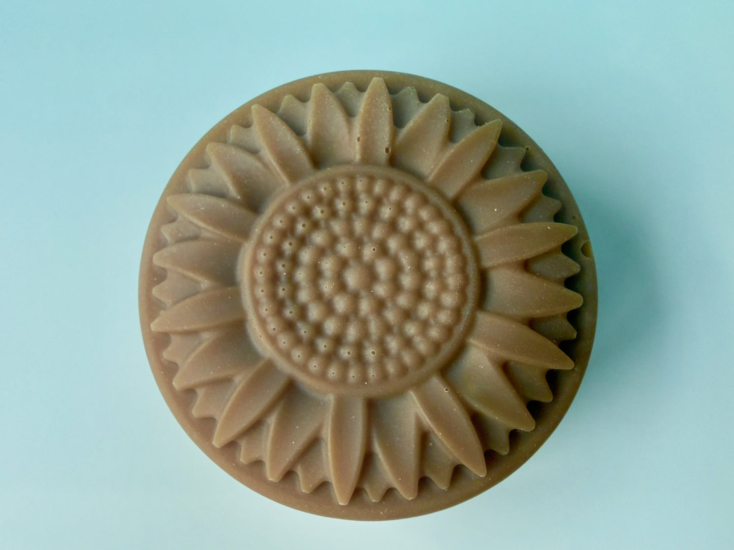 Round sunflower-shaped solid dish soap with raised petal detail and warm beige tone
