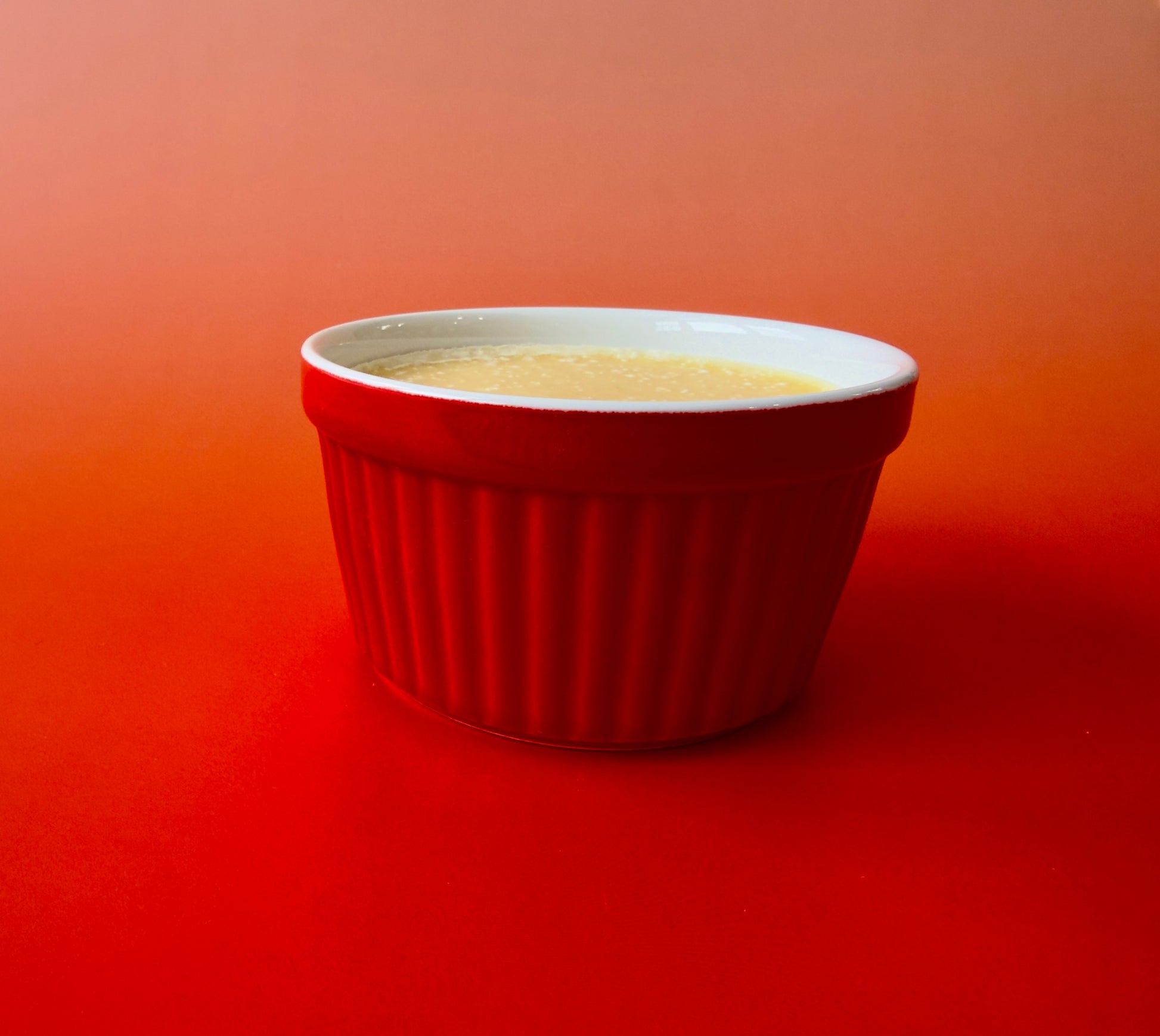 Solid dish soap poured into a red ceramic ramekin on a warm orange background
