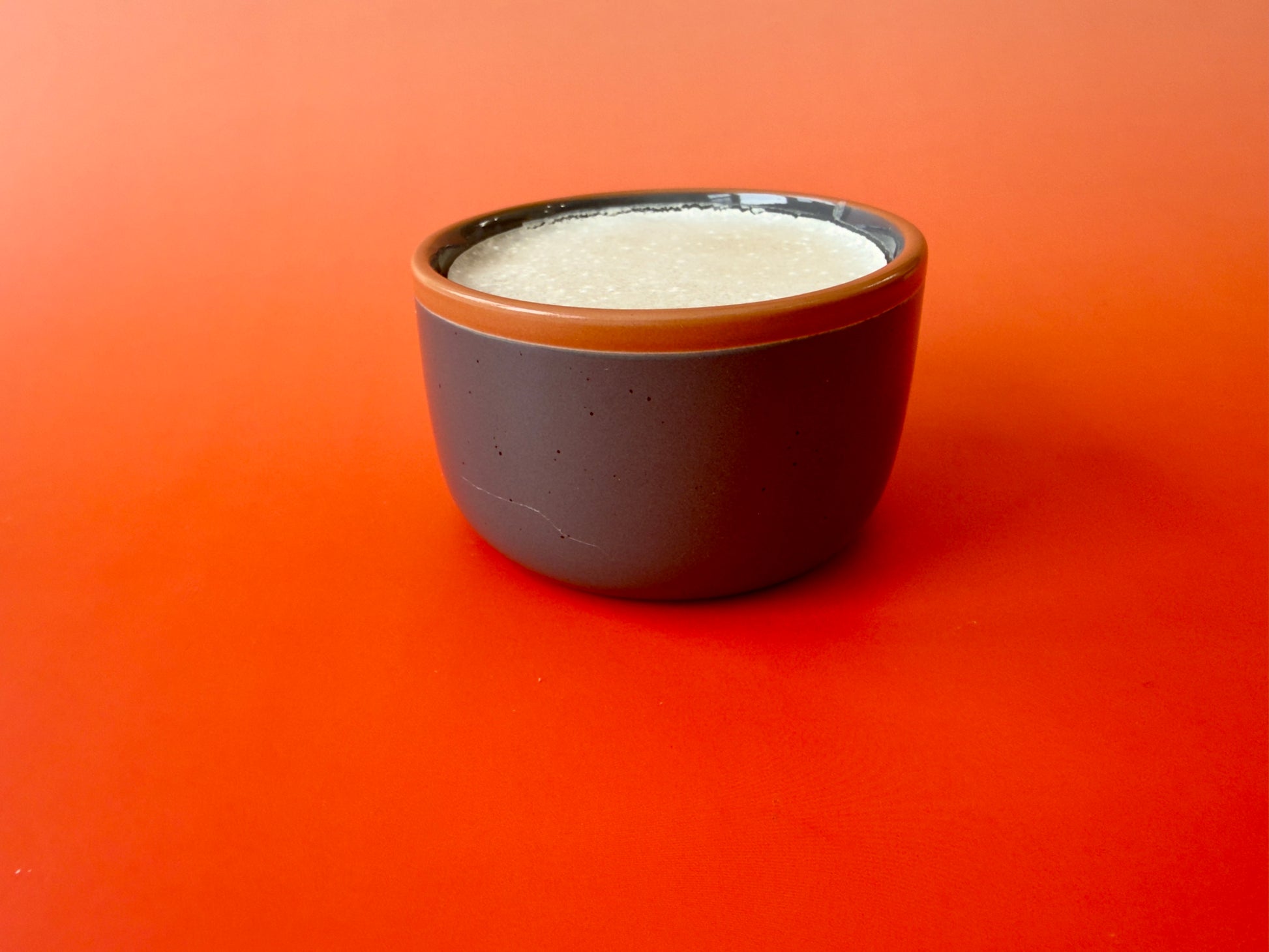 Solid dish soap poured into ceramic ramekin on a warm orange background