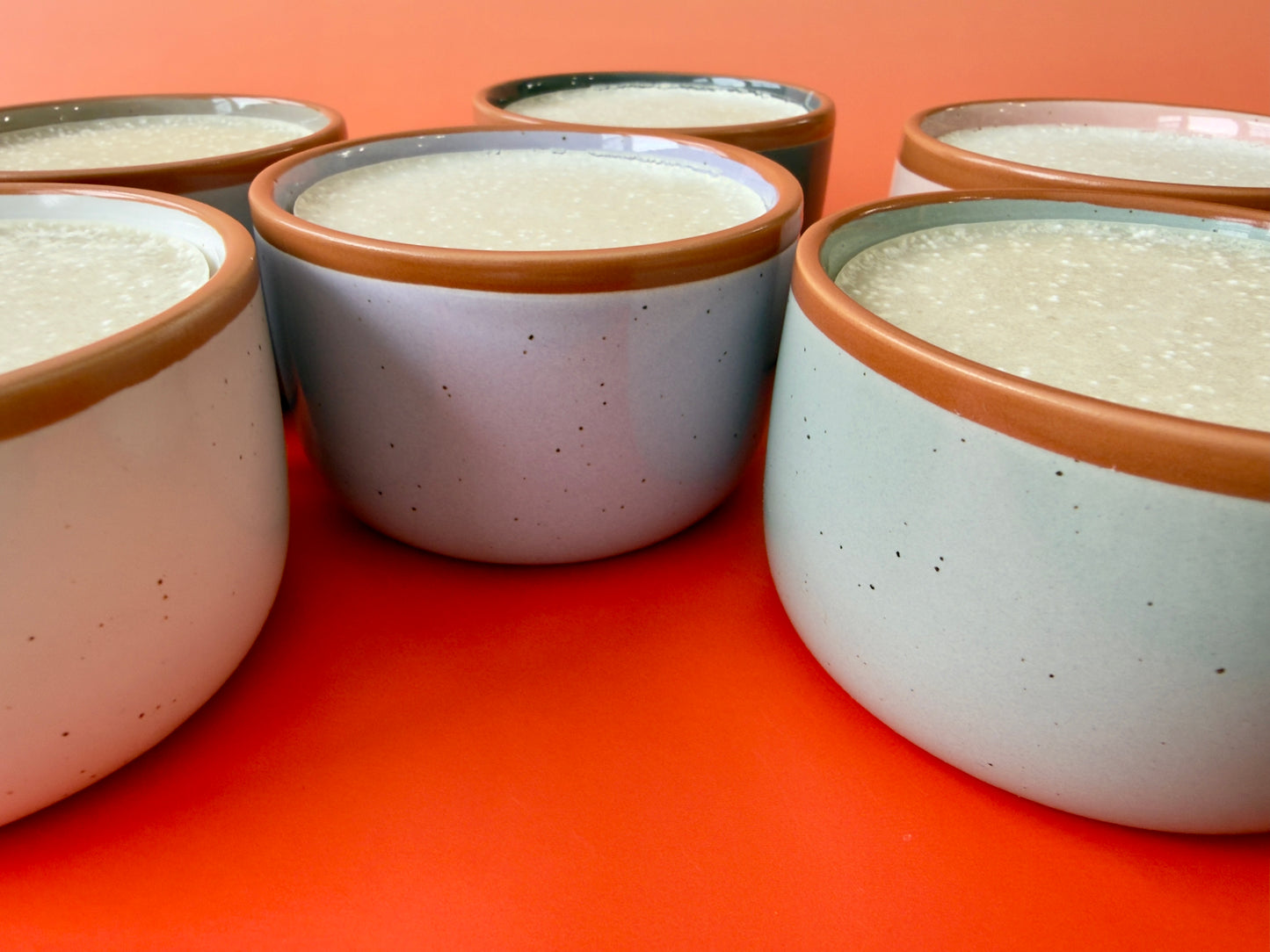 Group of solid dish soaps in assorted ceramic ramekins arranged on orange backdrop