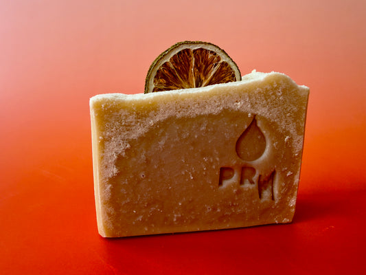 Mint + Grapefruit soap bar with PRM logo, topped with a dried lime slice, set against an orange gradient background
