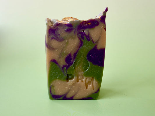 Tall bar of Orange Coconut Melon soap with purple and green hanger swirl on a light green background, PRM logo stamped on the front