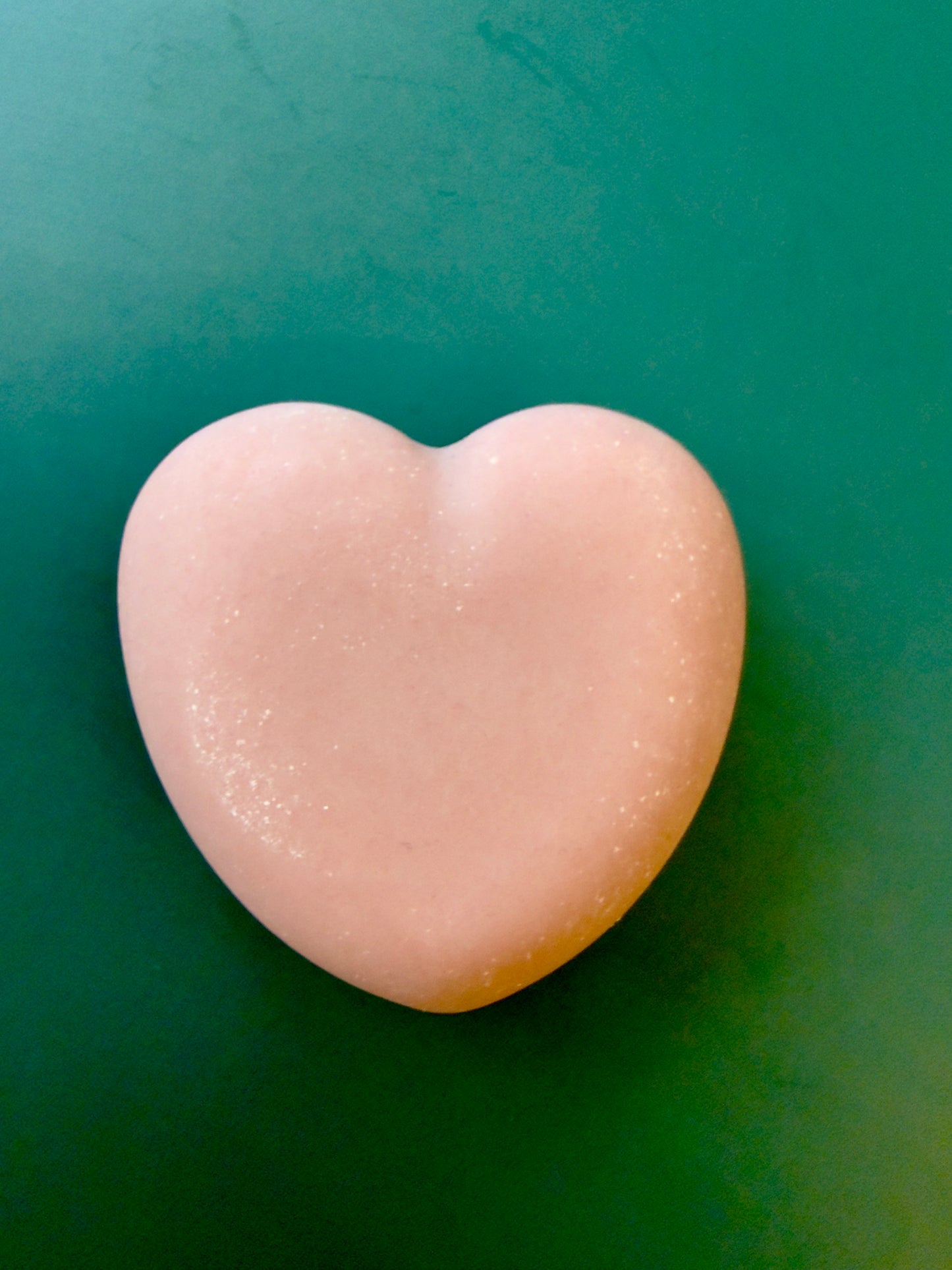 Tea Rose + Bergamot goat milk heart soap with a soft pink color on a green background.