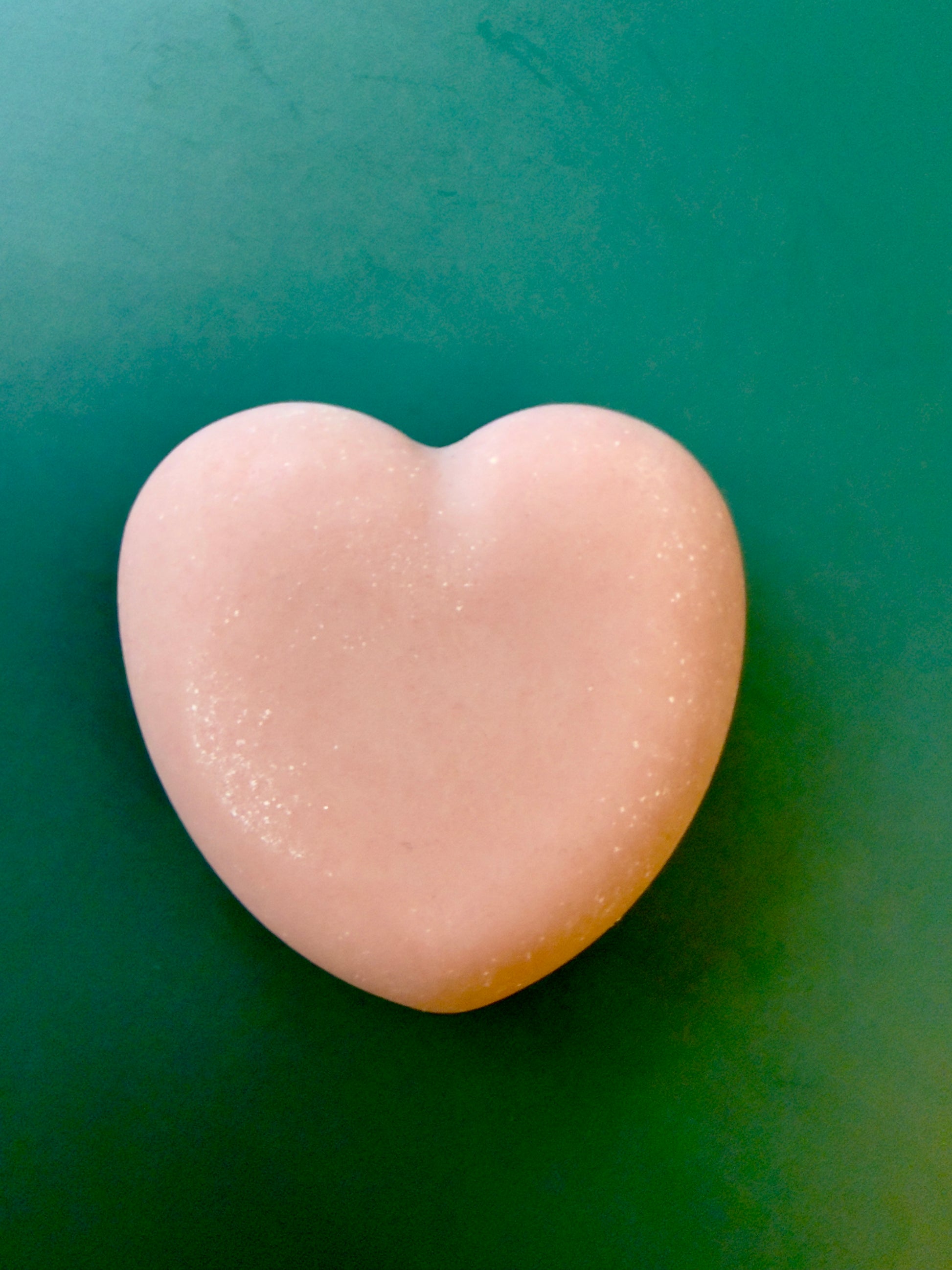Tea Rose + Bergamot goat milk heart soap with a soft pink color on a green background.