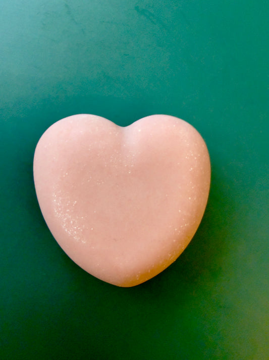 Tea Rose + Bergamot goat milk heart soap with a soft pink color on a green background.