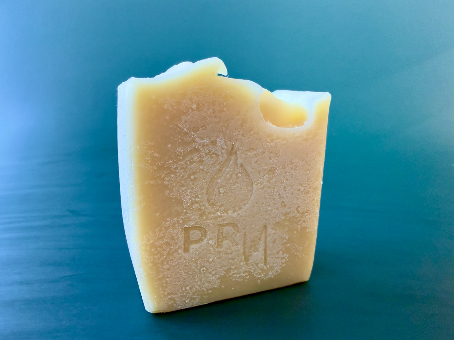 Lavender Orange small batch goat milk soap bar with PRM stamp on a dark teal background.