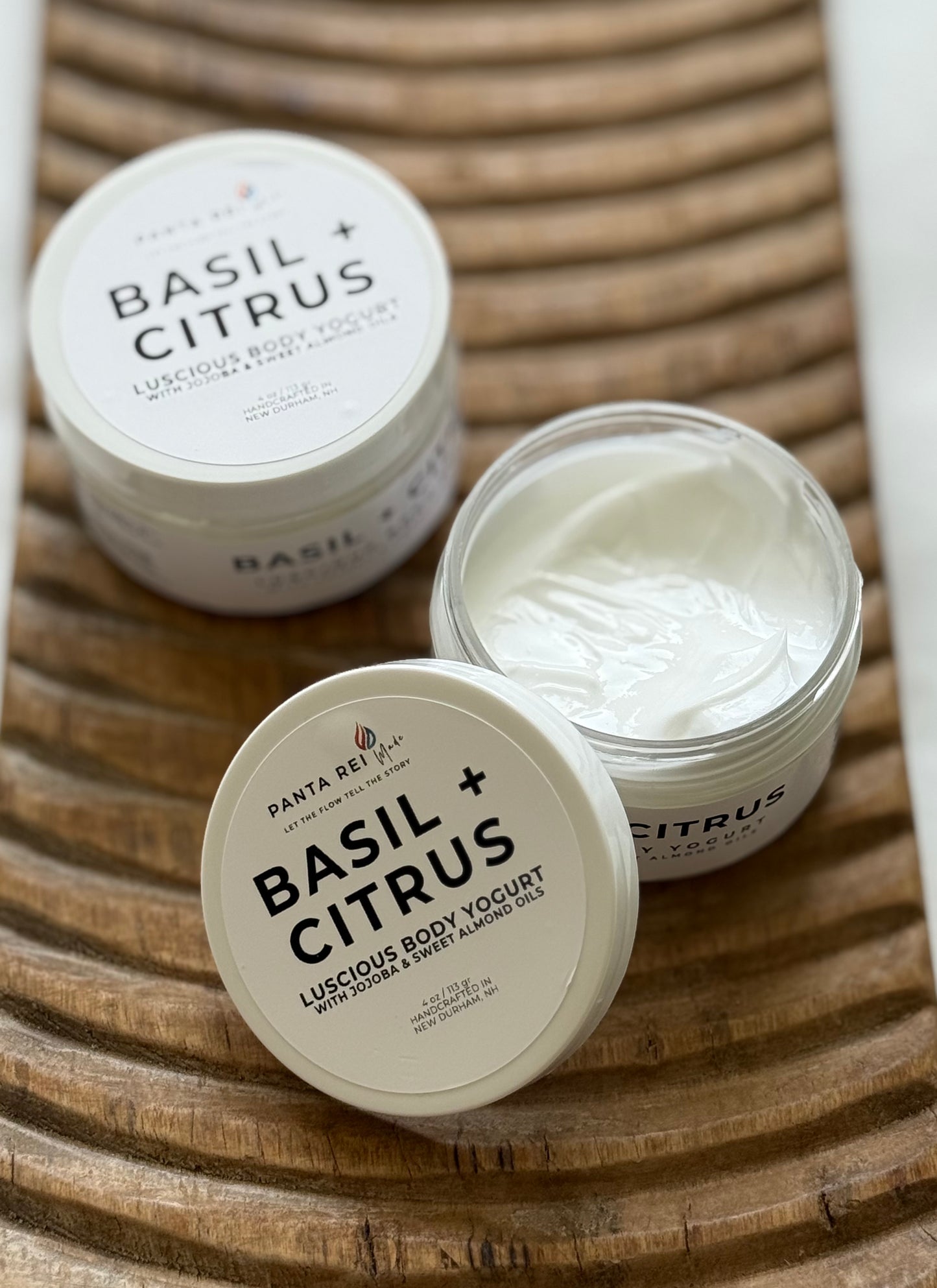 Basil + Citrus luscious body yogurt in white jars with white lids on a wooden tray.
