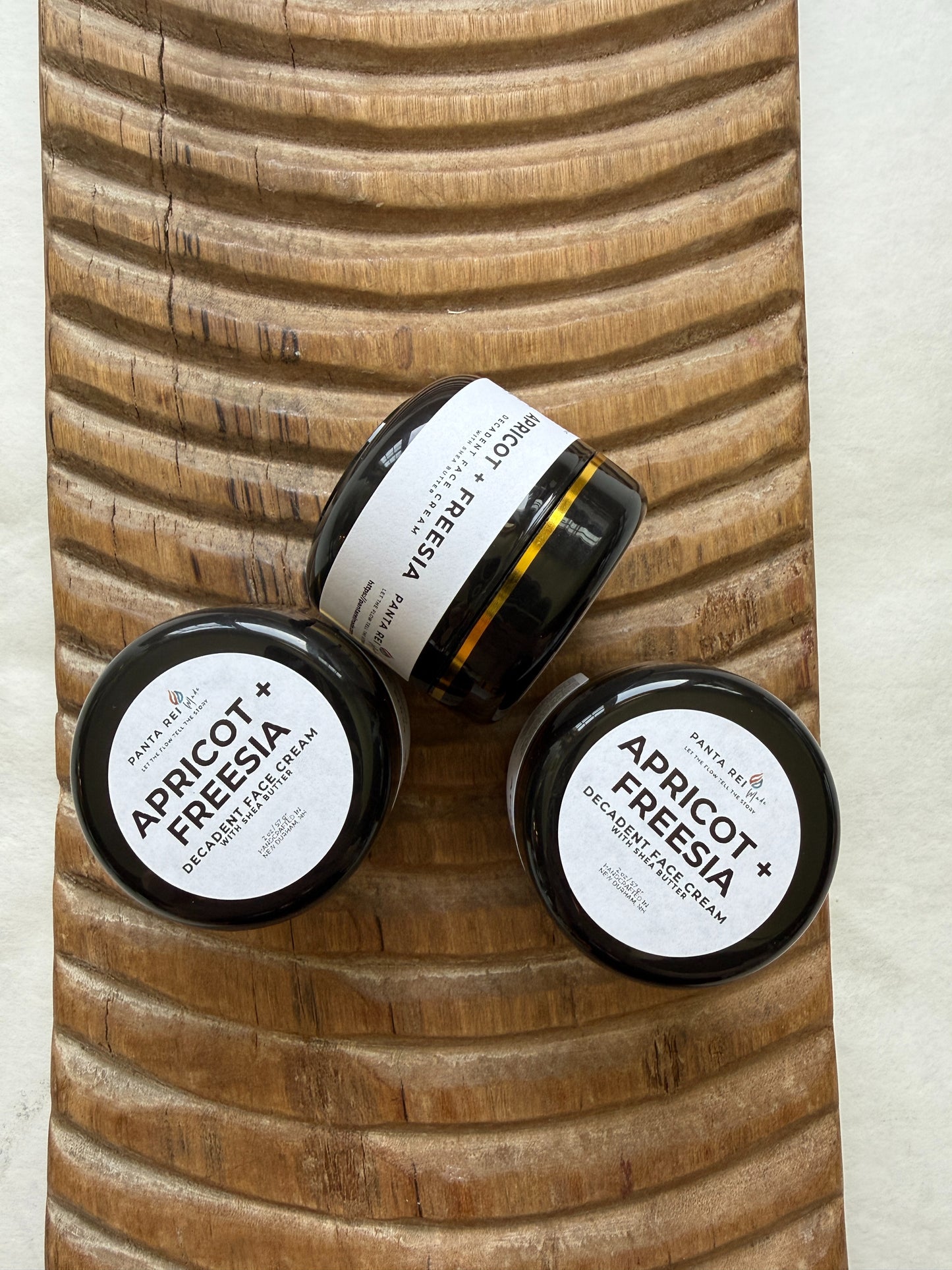 Three small jars of apricot freesia body scrub on a wooden surface