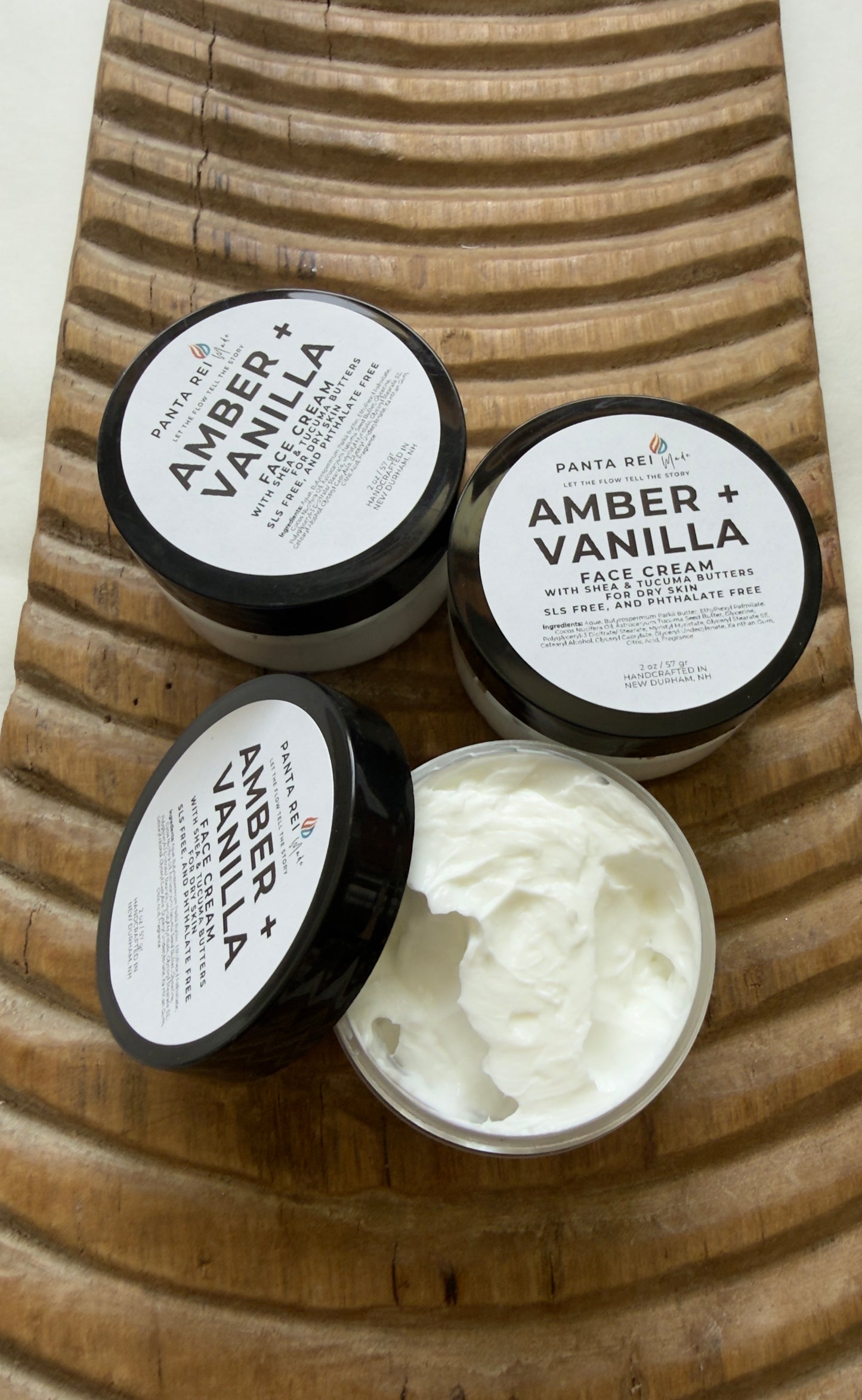 Three jars of 'Amber + Vanilla' face cream on a wooden surface.