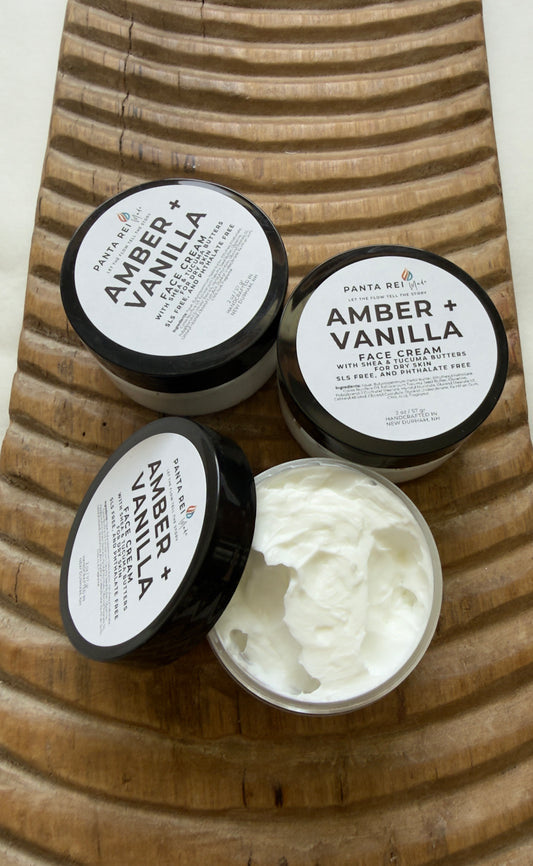 Three jars of 'Amber + Vanilla' face cream on a wooden surface.