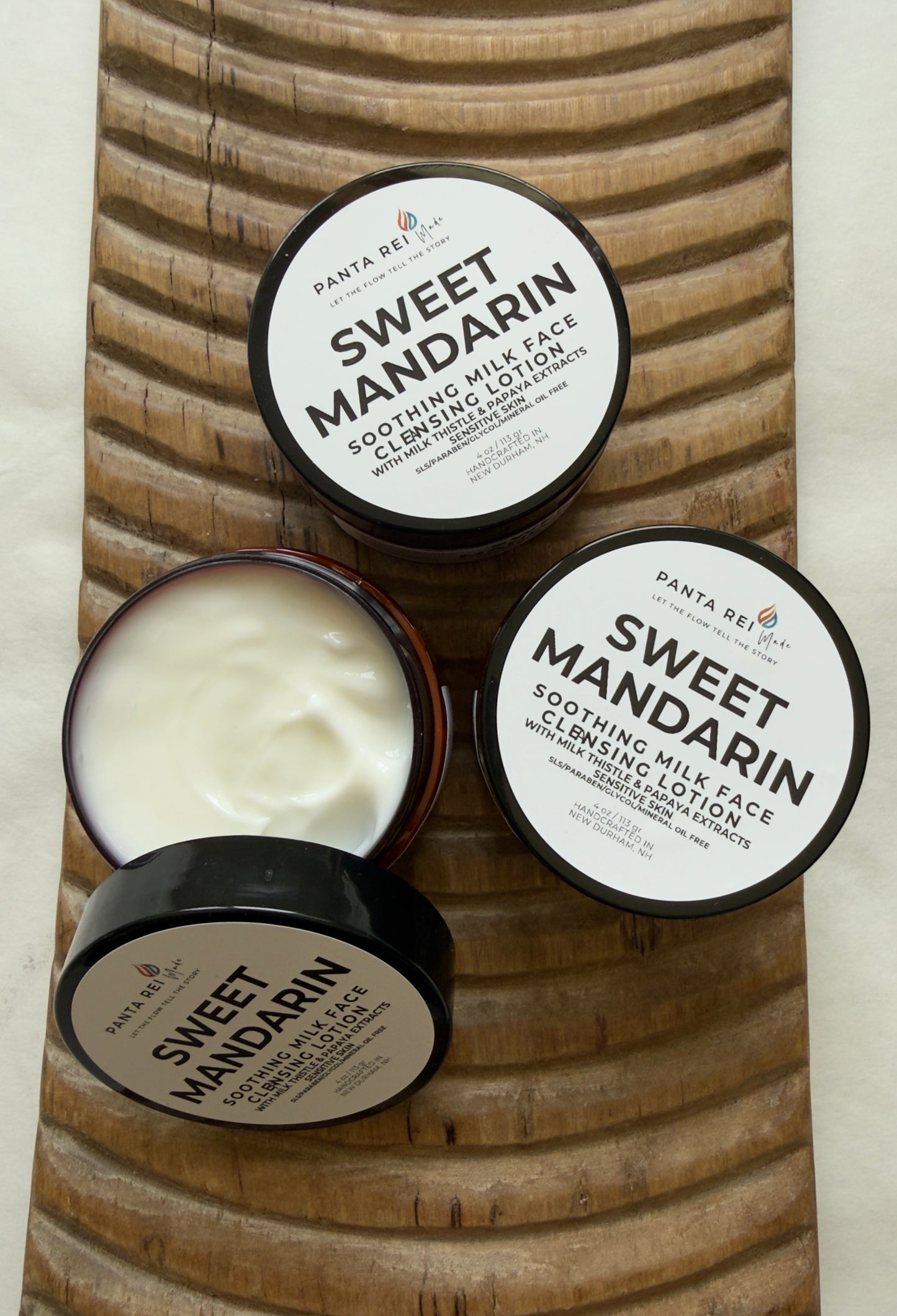 Three containers of 'Sweet Mandarin' cleansing lotion on a wooden surface