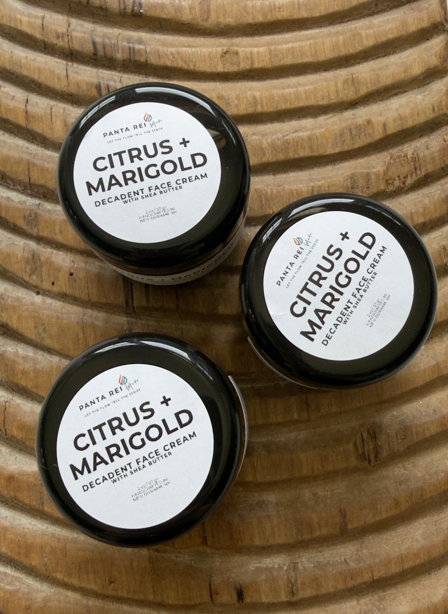 Three jars of Citrus + Marigold Decadent Face Cream on a wooden surface