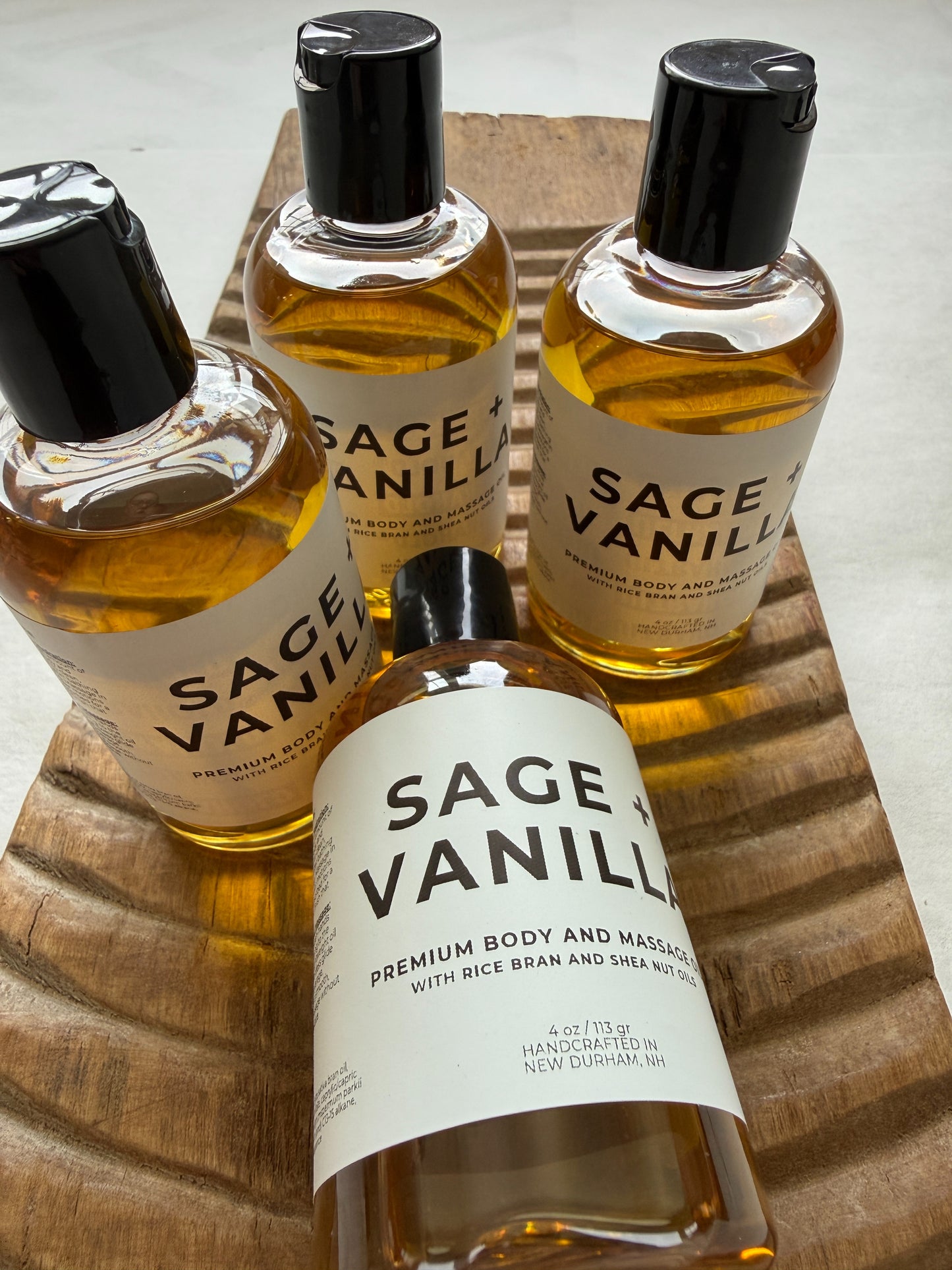 Four bottles of Sage Vanilla massage oil on a wooden surface