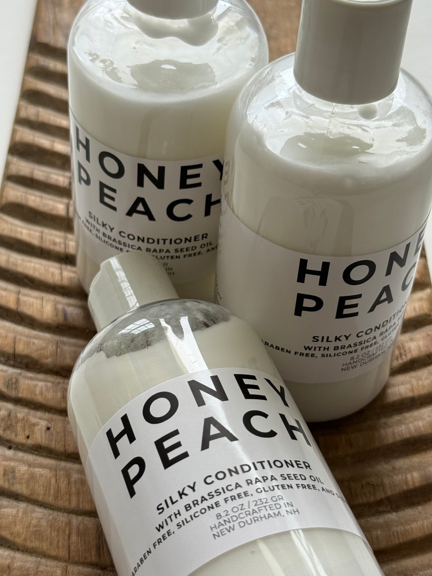 Three bottles of Honey Peach Silky Conditioner on a wooden surface