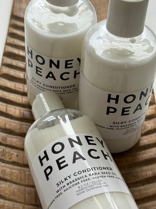 Three bottles of Honey Peach Silky Conditioner on a wooden surface