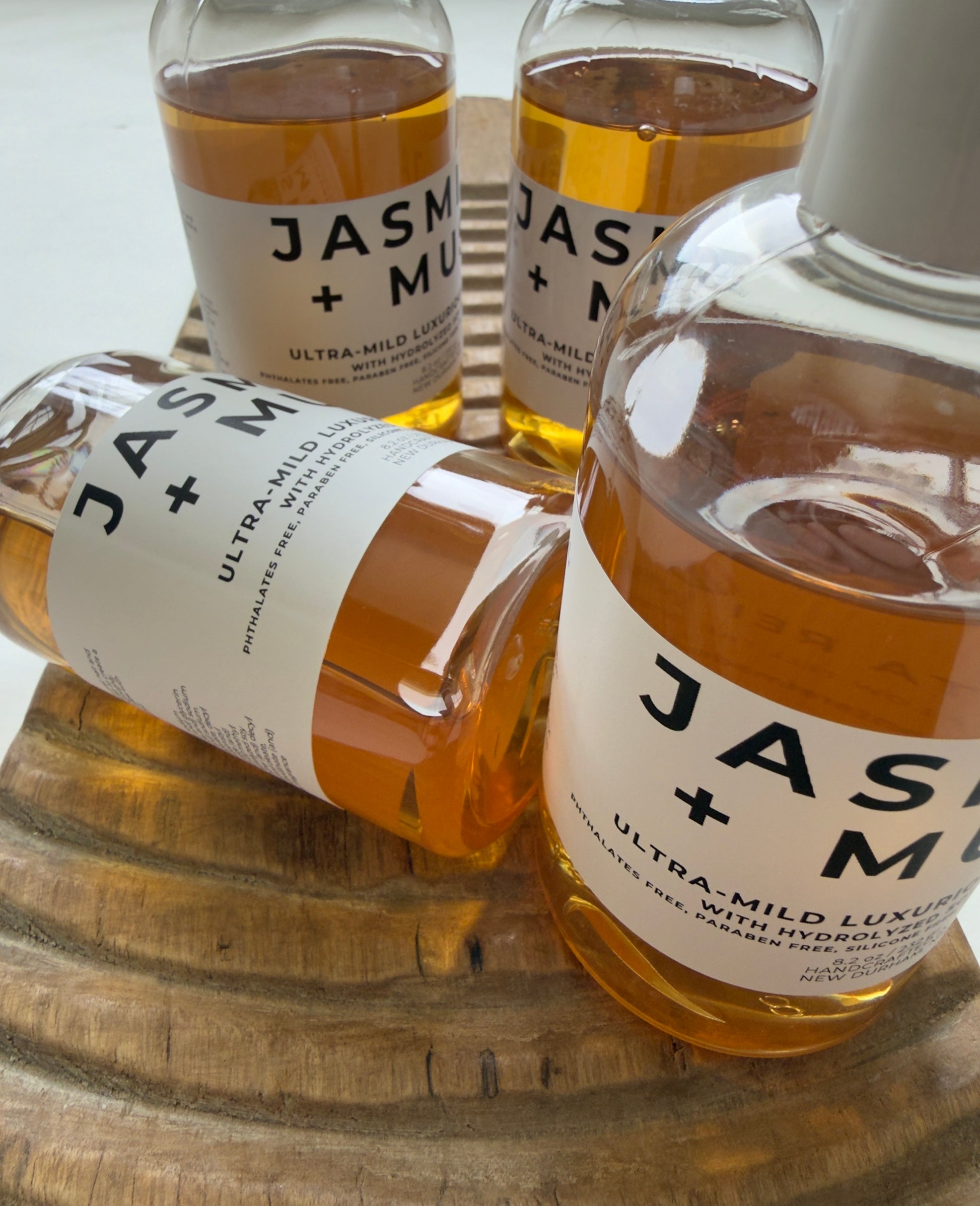 Jasmine + Musk ultra-mild shampoo bottles on a carved wooden tray.