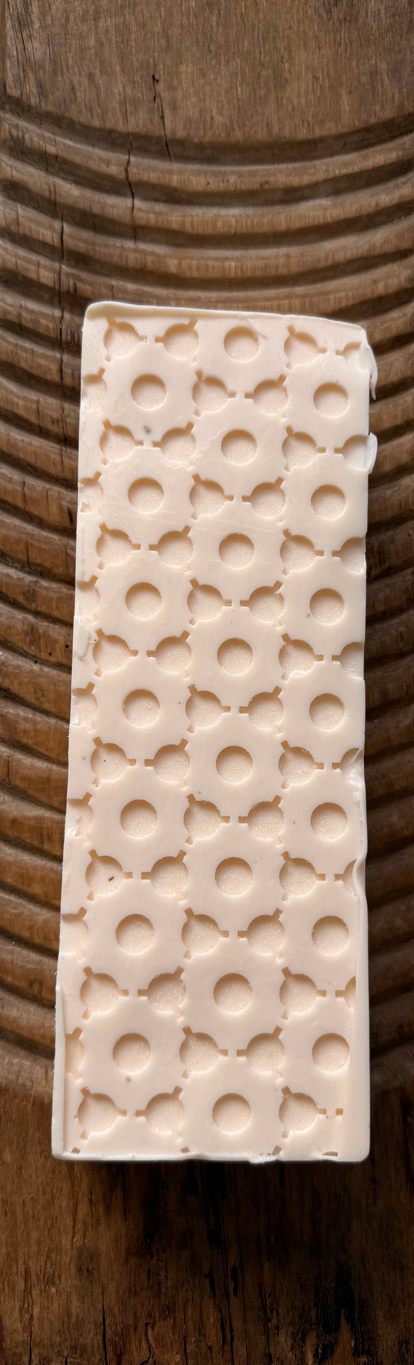 Rectangular white loaf of soap with circular patterns on a wooden surface