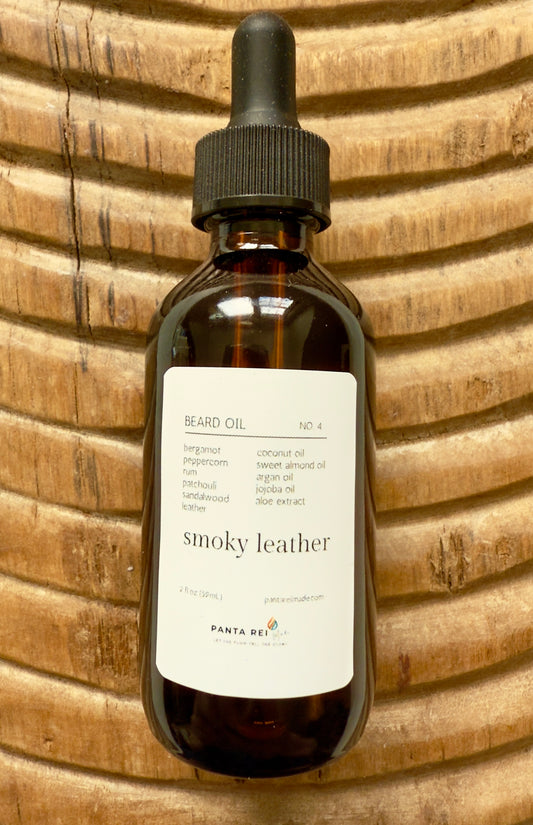 Amber bottle of Smoky Leather Beard Oil with a dropper cap, photographed on a carved wooden background.