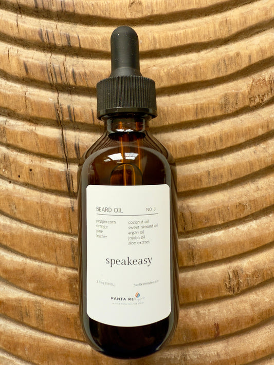 Amber bottle of Speakeasy Beard Oil with dropper cap, photographed on carved wood with warm natural lighting.