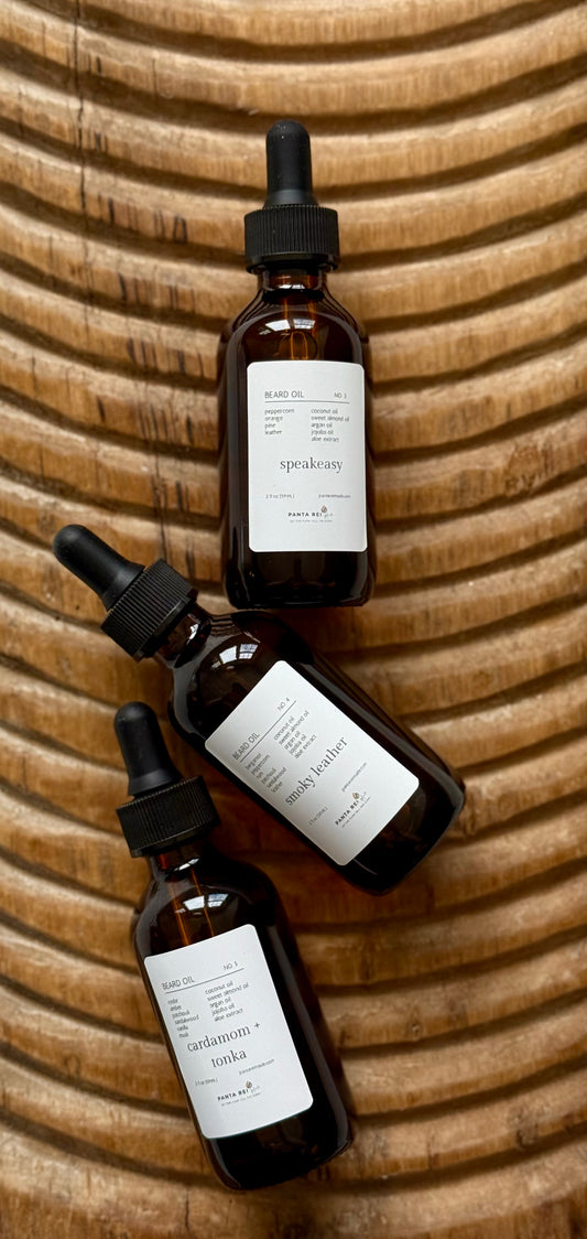 Three brown glass beard oil bottles with droppers on a textured wooden surface