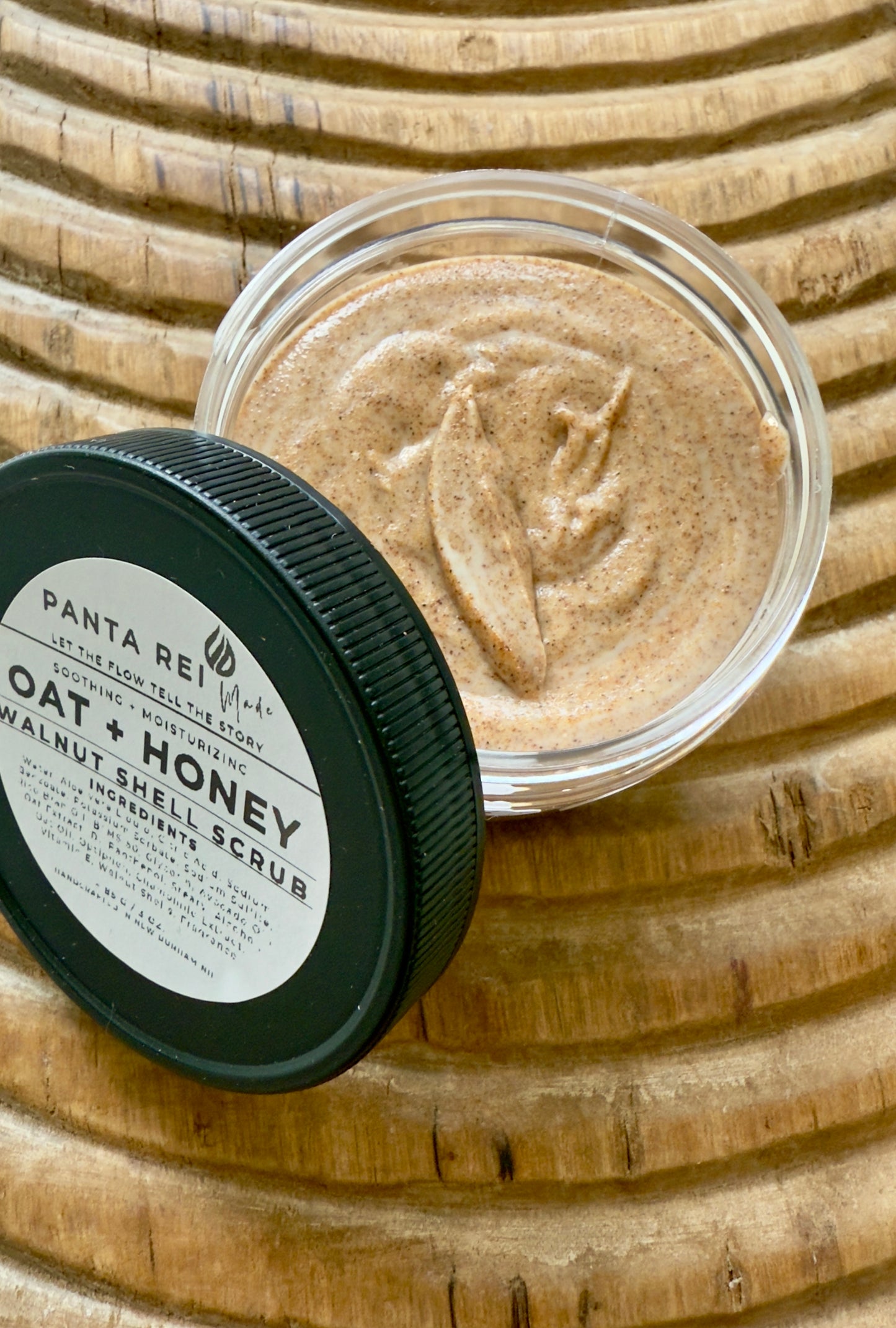 Top view of Oat + Honey Walnut Shell Scrub in a clear jar with black lid, showing creamy texture with fine walnut shell specks.