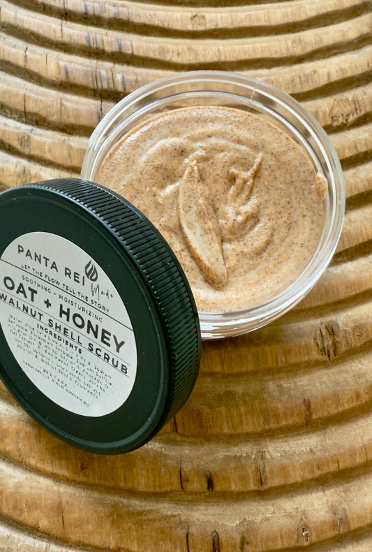 Top view of Oat + Honey Walnut Shell Scrub in a clear jar with black lid, showing creamy texture with fine walnut shell specks.