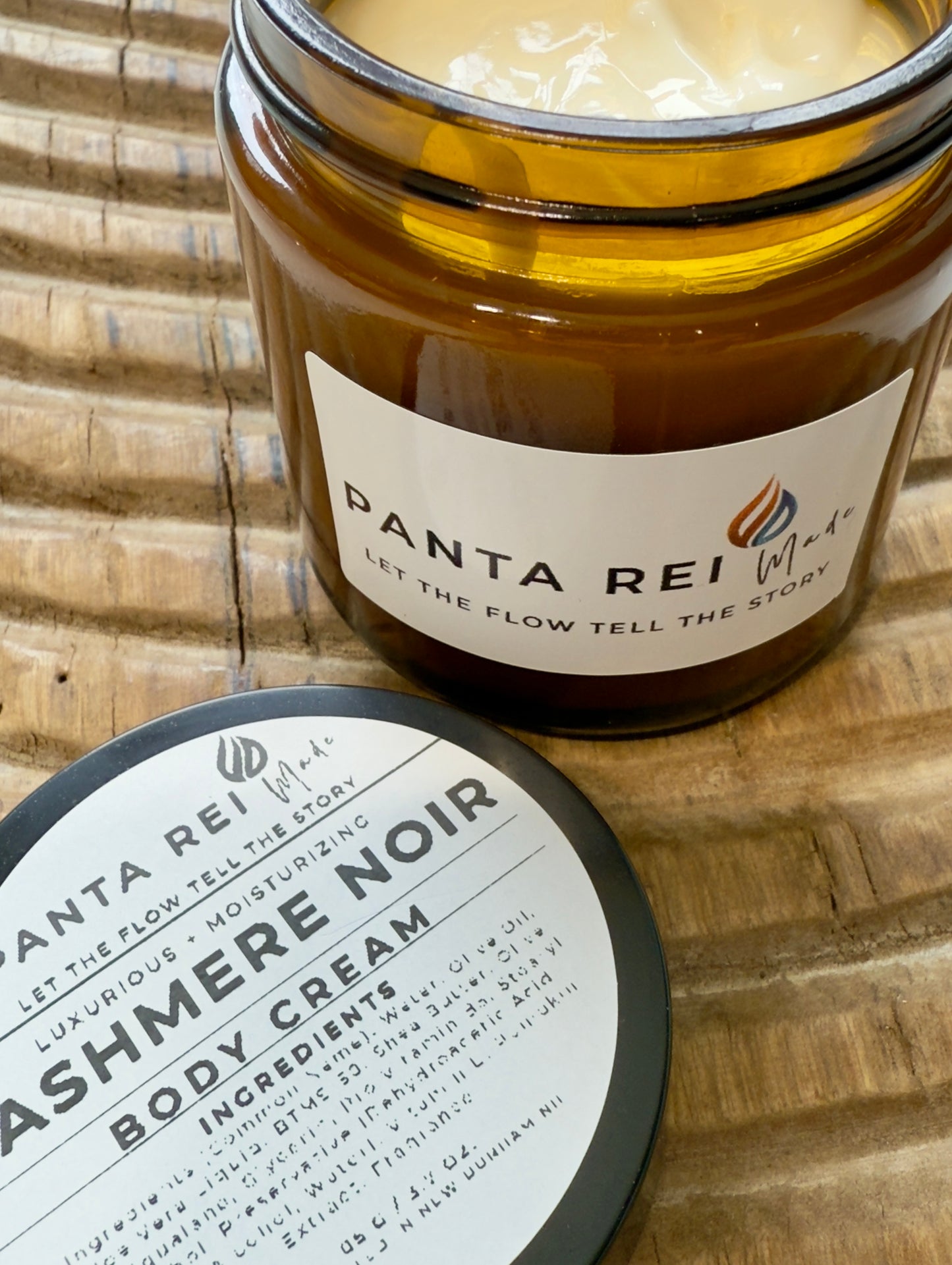 Amber-glass jar of Cashmere Noir Body Cream on carved wooden surface, shown open with creamy texture and matching lid.