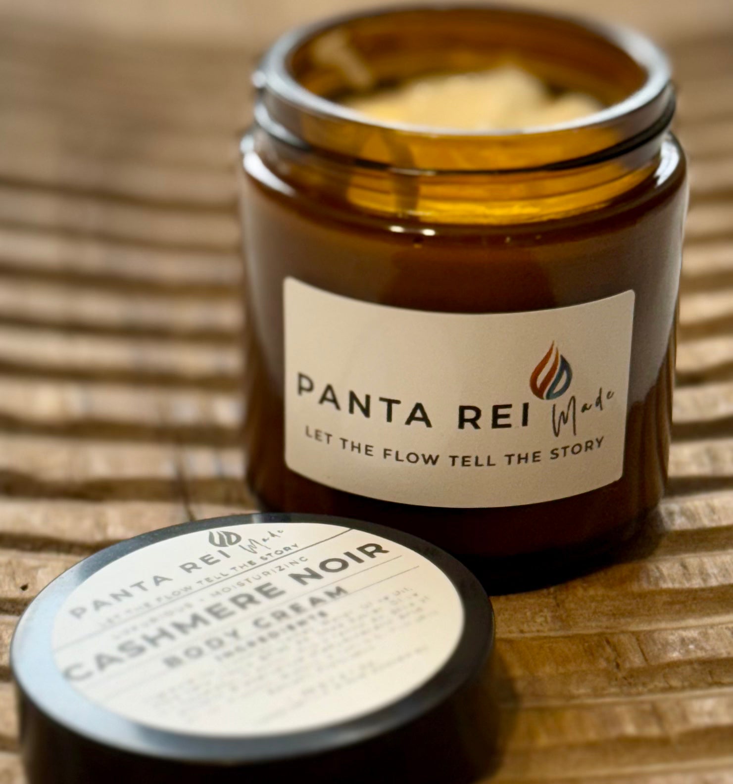 Amber-glass jar of Cashmere Noir Body Cream on carved wooden surface, shown open with creamy texture and matching lid.